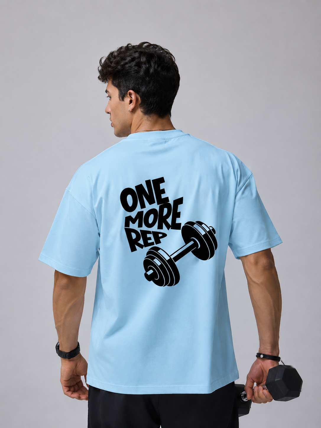 Man wearing blue oversized gym t-shirt with One More Rep dumbbell back graphic design.