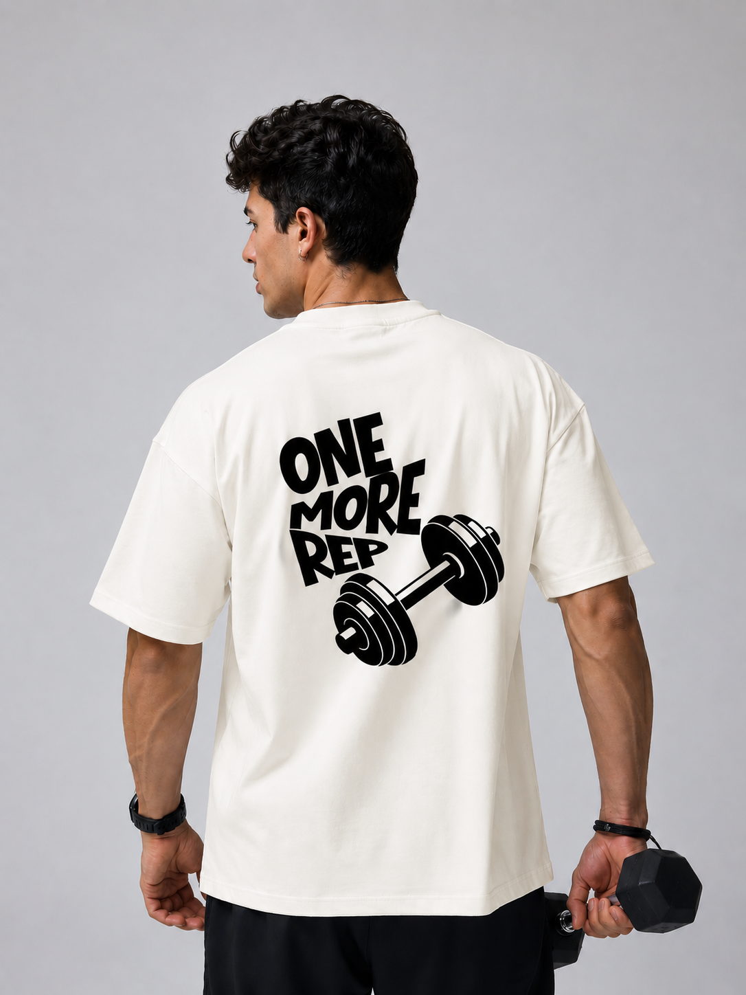 Man wearing off white oversized gym t-shirt with One More Rep dumbbell back graphic design.