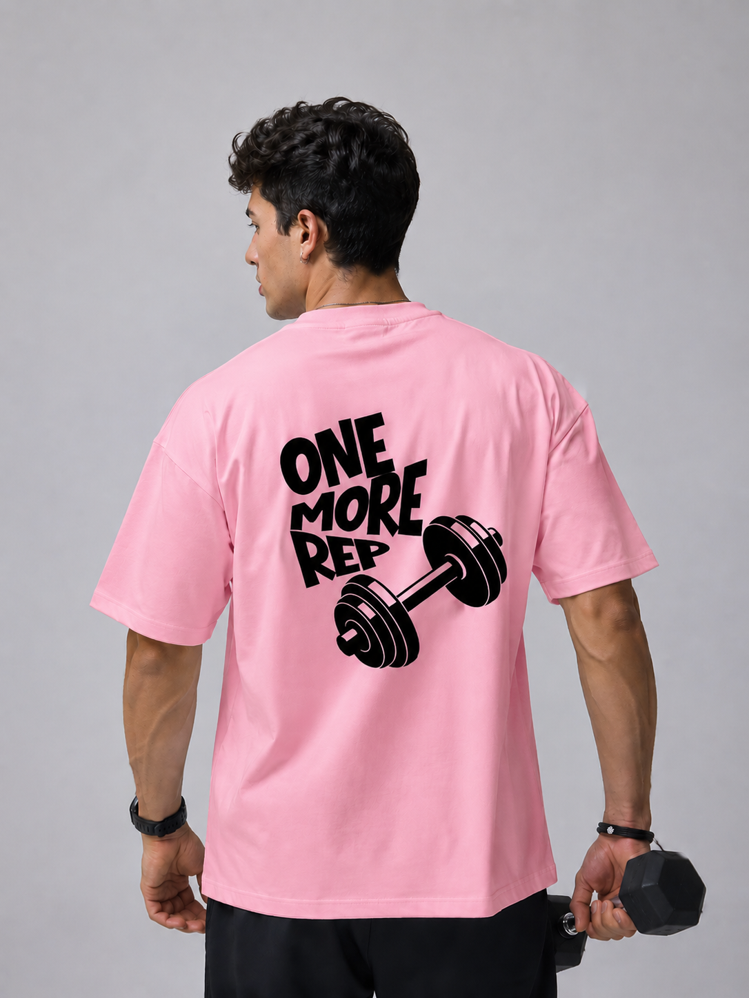 Man wearing pink oversized gym t-shirt with One More Rep dumbbell back graphic design.